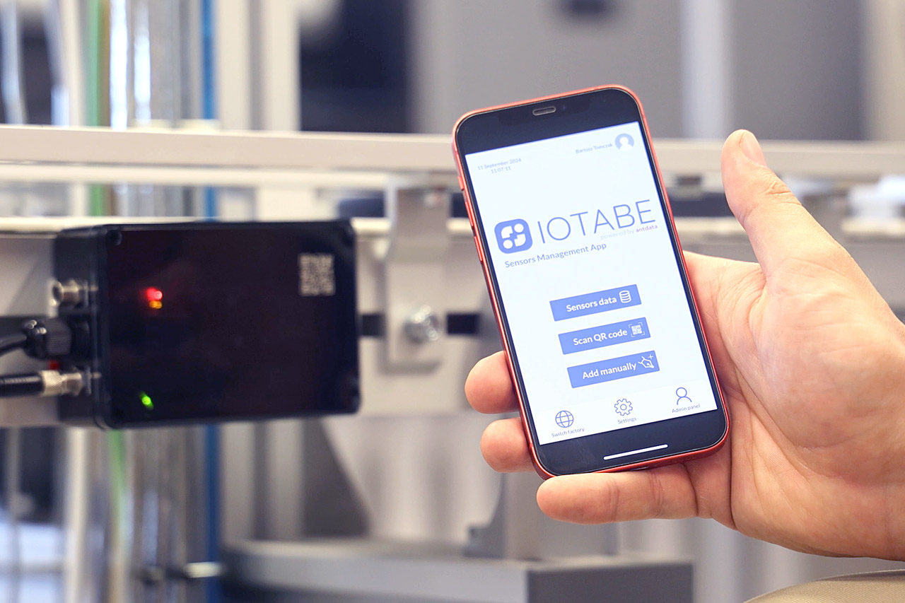 IoTabe sensor management app displayed on a smartphone next to industrial equipment